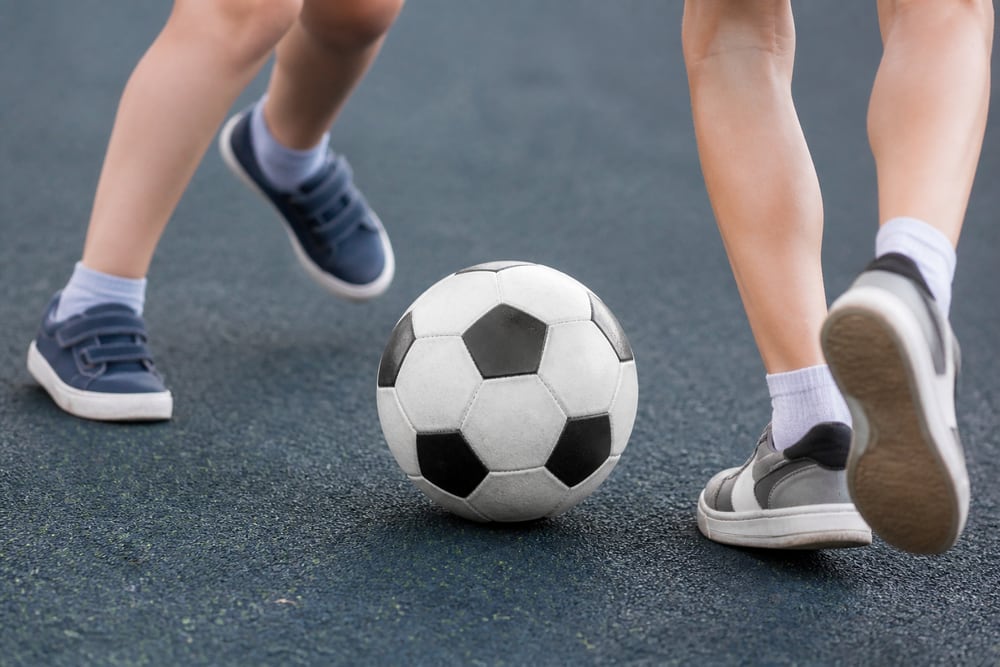 Ilustračný detail celej futbalovej lopty a detských nôh v pohybe.
